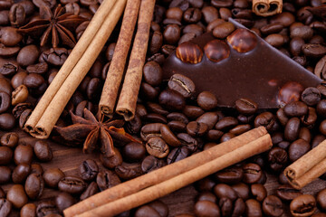 Chocolate bar with nuts on a wooden table with coffee beans and spices. Roasted coffee beans, cinnamon sticks and anise stars. Macro shot.