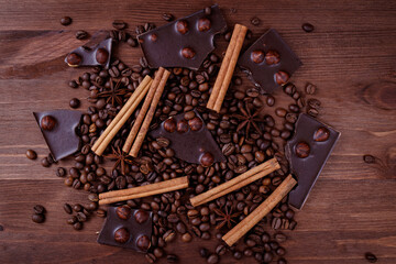 Chocolate bar with nuts on a wooden table with coffee beans and spices. Roasted coffee beans, cinnamon sticks and anise stars. Top view.