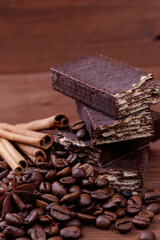 Wafer bars covered with chocolate on a dark wooden background with coffee beans, cinnamon sticks and anise stars. Wafer bars stack. Macro shot.