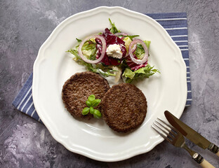 Fried mince patties, also know as rissoles. The side dish is a Greek style salad with colorful vegetables, mixed greens, red onions, cucumber, tomato, crumbly feta cheese and vinaigrette.