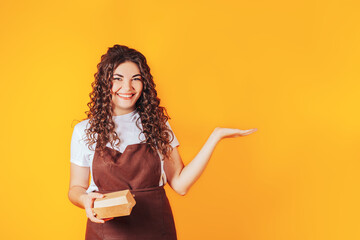 Young woman dressed in a catering uniform with outstretched arms, boxes of food in hands