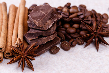 Stack of chocolate bar pieces with heap of roasted coffee beans and spices, cinnamon sticks and...