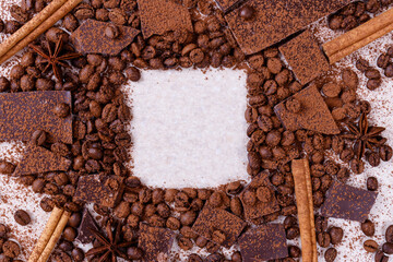 Pieces of chocolate bar on a white table with roasted coffee beans and spices, cinnamon sticks and...