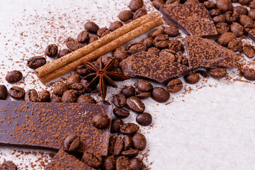 Pieces of chocolate bar on a white table with roasted coffee beans and spices, cinnamon sticks and anise stars, covered with cocoa powder. Copy space in the corner in circle form.