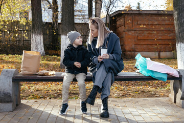 Beautiful young mother of 30 years with a child of 5 years sitting on a bench in the Park. Eat and drink coffee in the autumn Park