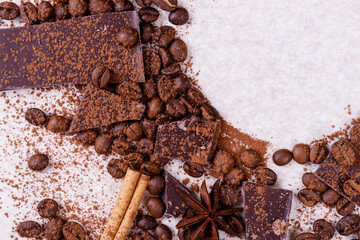 Pieces of chocolate bar on a white table with roasted coffee beans and spices, cinnamon sticks and anise stars, covered with cocoa powder. Copy space in the corner in circle form. Top view.