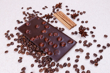 Chocolate bar with nuts on a white table with coffee beans and spices. Roasted coffee beans,...