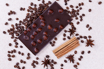 Chocolate bar with nuts on a white table with coffee beans and spices. Roasted coffee beans, cinnamon sticks and anise stars. Chocolate bar with hazelnuts. Top view.