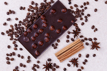 Chocolate bar with nuts on a white table with coffee beans and spices. Roasted coffee beans,...