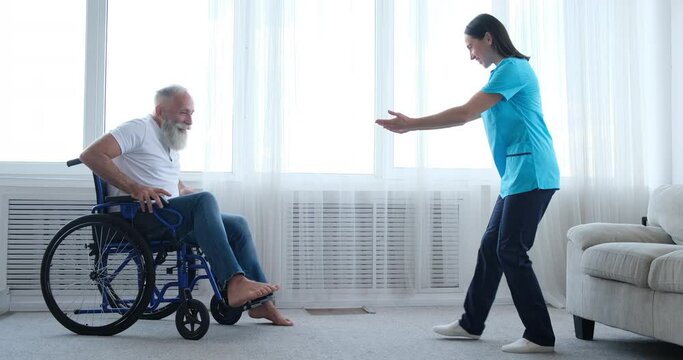Female nurse encouraging and helping disabled old man to get out of the wheelchair