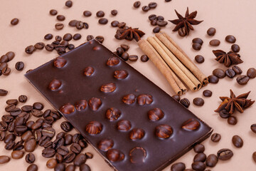 Chocolate bar with nuts on the beige background with coffee beans and spices. Roasted coffee beans, cinnamon sticks and anise stars. Chocolate bar with hazelnuts. 
