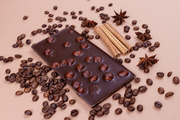 Chocolate bar with nuts on the beige background with coffee beans and spices. Roasted coffee beans, cinnamon sticks and anise stars. Chocolate bar with hazelnuts. 