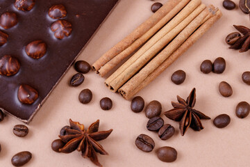 Chocolate bar with nuts on the beige background with coffee beans and spices. Roasted coffee beans, cinnamon sticks and anise stars. Chocolate bar with hazelnuts. 