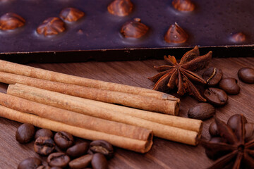 Chocolate bar with nuts on a wooden table with coffee beans and spices. Roasted coffee beans, cinnamon sticks and anise stars. Chocolate bar with hazelnuts. 