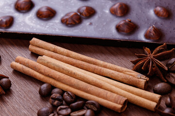 Chocolate bar with nuts on a wooden table with coffee beans and spices. Roasted coffee beans, cinnamon sticks and anise stars. Chocolate bar with hazelnuts. 