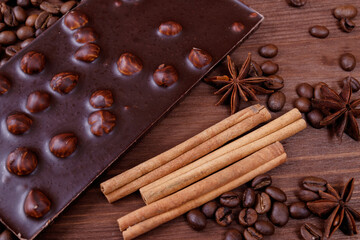 Chocolate bar with nuts on a wooden table with coffee beans and spices. Roasted coffee beans, cinnamon sticks and anise stars. Chocolate bar with hazelnuts. 