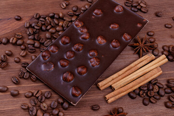 Chocolate bar with nuts on a wooden table with coffee beans and spices. Roasted coffee beans, cinnamon sticks and anise stars. Chocolate bar with hazelnuts. 