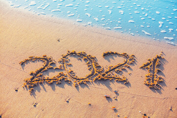 Happy New Year concept. Inscription 2021 written on the sandy beach with wave