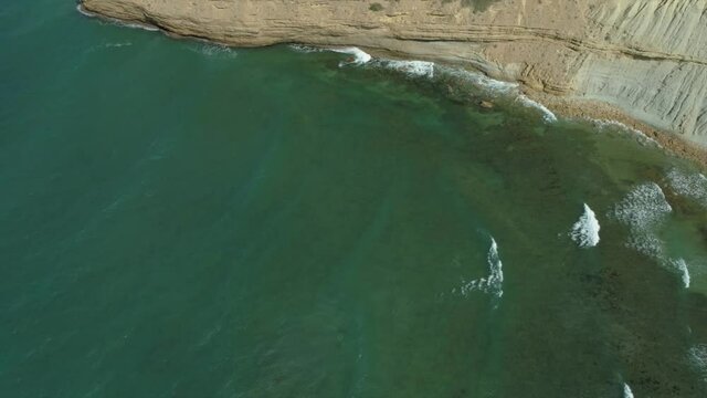 Beautiful turquoise ocean water waves crash agains huge ocean coastal cliffs, drone aerial
