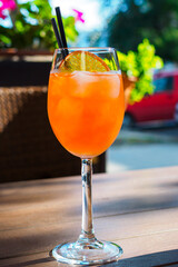 aperol spritz with orange slice and two black straws on wooden table