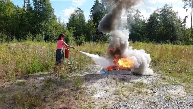 Young Woman Putting Out A Large Fire At A Firefighting Training. Beautiful Slow Motion Mobile Phone Video.