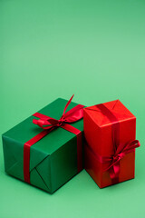 two colorful gift boxes with red ribbons and bows on green background