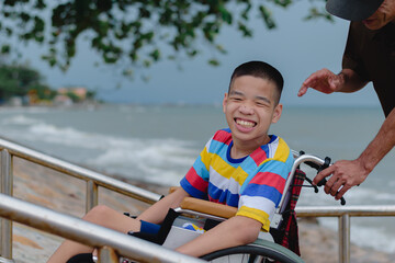 Asian special child on wheelchair is smiling,doing activity make funny face on the sea beach, Lifestyle of disability child, Life in the education age, Happy disabled kid in travel holidays concept...