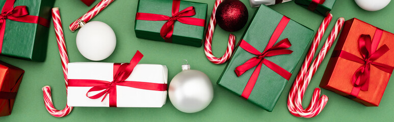panoramic concept of colorful gift boxes, candy canes and christmas balls on green background, top view