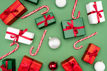 top view of colorful gift boxes, candy canes and christmas balls on green background