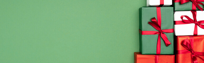 top view of colorful gift boxes with red ribbons on green background, website header