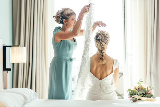 Beautiful Blonde-haired Woman Dressed In White On Her Wedding Day Before Getting Married, Her Mother Helps Her To Dress.