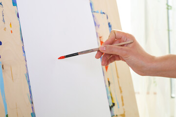 the artist's hand holds a brush on the background of the easel with paper