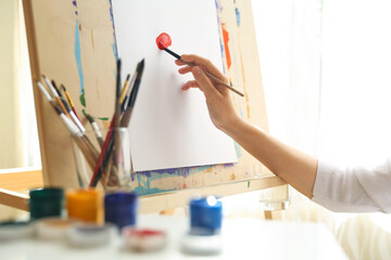 the artist's hand holds a brush on the background of the easel with paper
