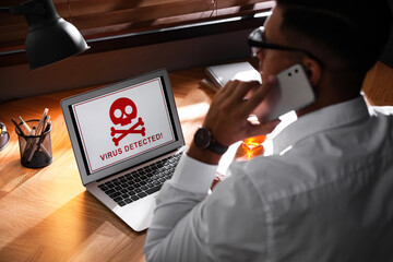 Man in front of laptop with warning about virus attack at workplace