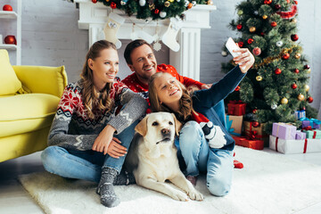 girl taking selfie with joyful parents and dog in decorated living room