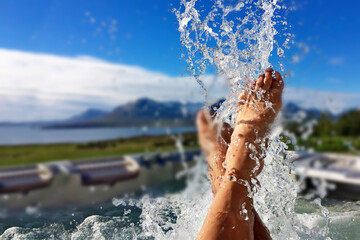 Splashes of water from the feet of a male tourist in a bath in the open air at sunrise against the backdrop of mountains in Iceland