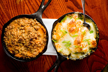 Steakhouse side dishes. Asparagus, salad, tomatoes, mashed potatoes, red onions, cream cauliflower, pickled peppers, seasoned meats served in cast iron skillet. Traditional appetizer items.