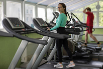 Fototapeta na wymiar A young athletic woman walks or runs on a treadmill in a fitness room.Workout and Strength training theme. Cardio training. Healthy and Exercise activity concept.