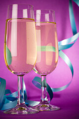 Studio photo of shiny champagne glasses with blue ribbons on pink and purple background