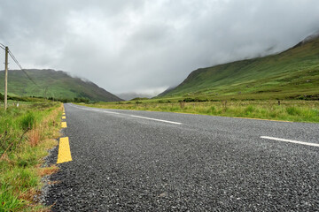 Narrow empty asphalt road into mountains, Low cloudy sky over peaks. Nobody, Connemara, Ireland. Concept travel, road trip