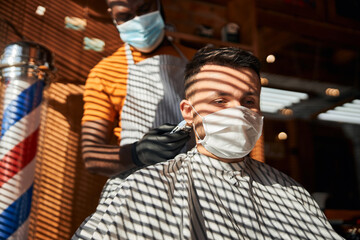 Handsome man in medical mask getting haircut in barbershop