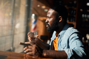 Bearded Afro American man smoking cigar and drinking whisky