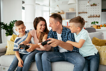 Husband and wife playing video games with joysticks in living room. Loving couple are playing video games with kids at home..