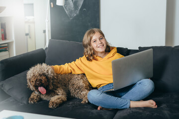 teenage girl sitting on sofa and playing with her dog at home