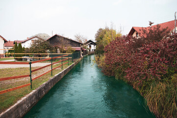 Fototapeta na wymiar Small river goes in village between houses, autumn season time. Deep water.