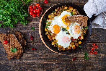 Fried eggs with vegetables  - shakshuka in a frying pan and rye bread on an old wooden background. Late breakfast. Rustic style. Middle eastern traditional dish.  Flat lay. Top view