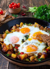 Fried eggs with vegetables  - shakshuka in a frying pan and rye bread on an old wooden background. Late breakfast. Rustic style. Middle eastern traditional dish