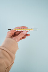 Caucasian woman hand holding a thermometer on a blue background.