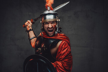 Screaming and assaulting mad roman warrior in armour and red mantle holding sword and shield in...