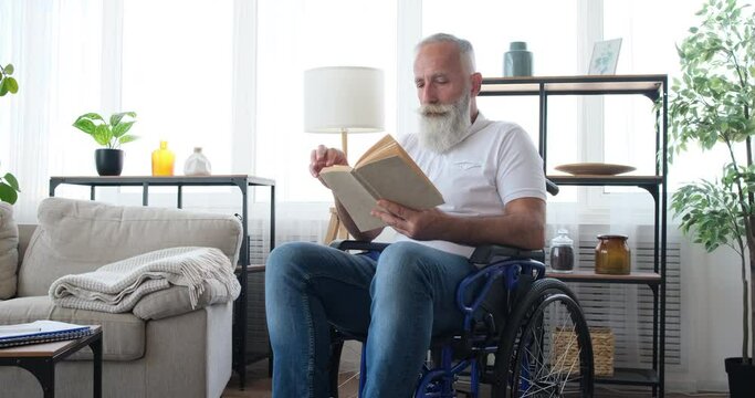 Handicap senior man in thoughts while reading a book sitting on wheelchair at home